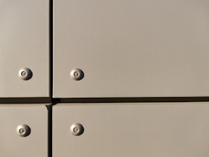 A close-up view of a section of a metal surface, featuring four screws with evenly spaced, flat panels. The panels are a light tan color with a slightly reflective finish, and they are arranged in a grid with visible seams.