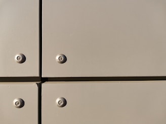 A close-up view of a section of a metal surface, featuring four screws with evenly spaced, flat panels. The panels are a light tan color with a slightly reflective finish, and they are arranged in a grid with visible seams.