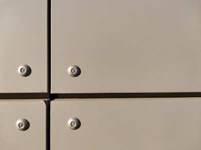 A close-up view of a section of a metal surface, featuring four screws with evenly spaced, flat panels. The panels are a light tan color with a slightly reflective finish, and they are arranged in a grid with visible seams.