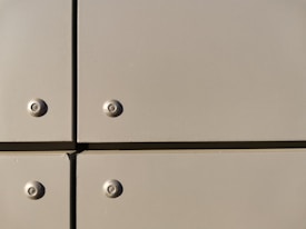 A close-up view of a section of a metal surface, featuring four screws with evenly spaced, flat panels. The panels are a light tan color with a slightly reflective finish, and they are arranged in a grid with visible seams.