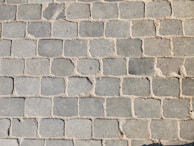 A pattern of rectangular stone pavers arranged in a grid, with varying shades of gray and beige grout filling the gaps between the stones.