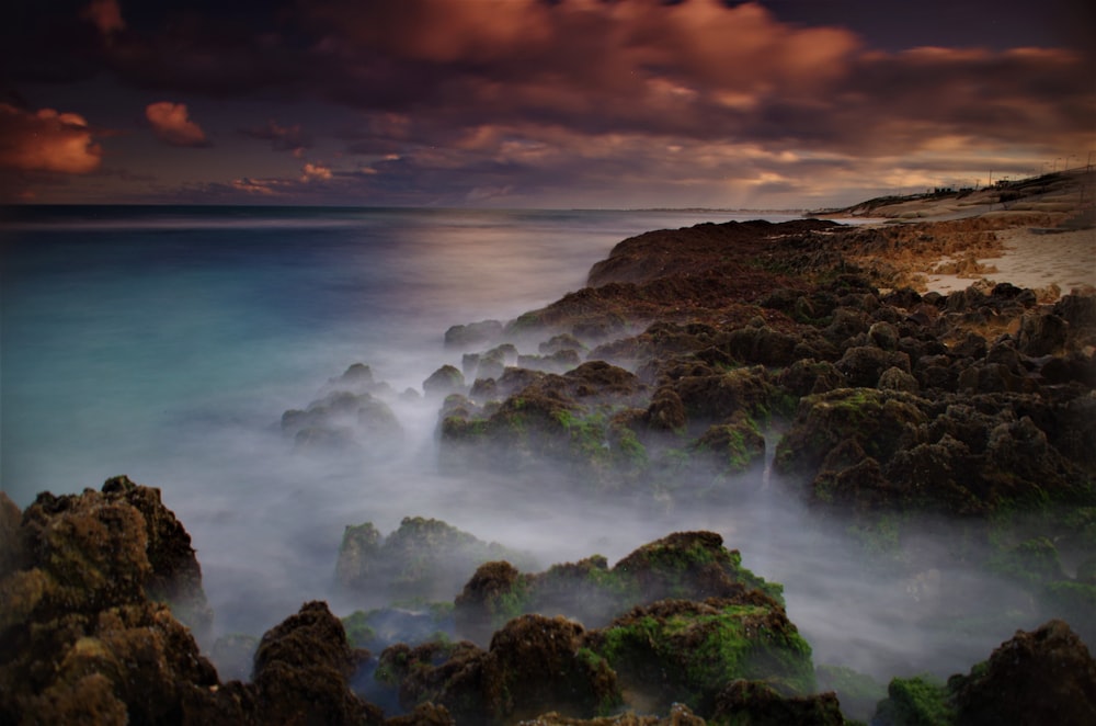 a rocky beach with a body of water in the background