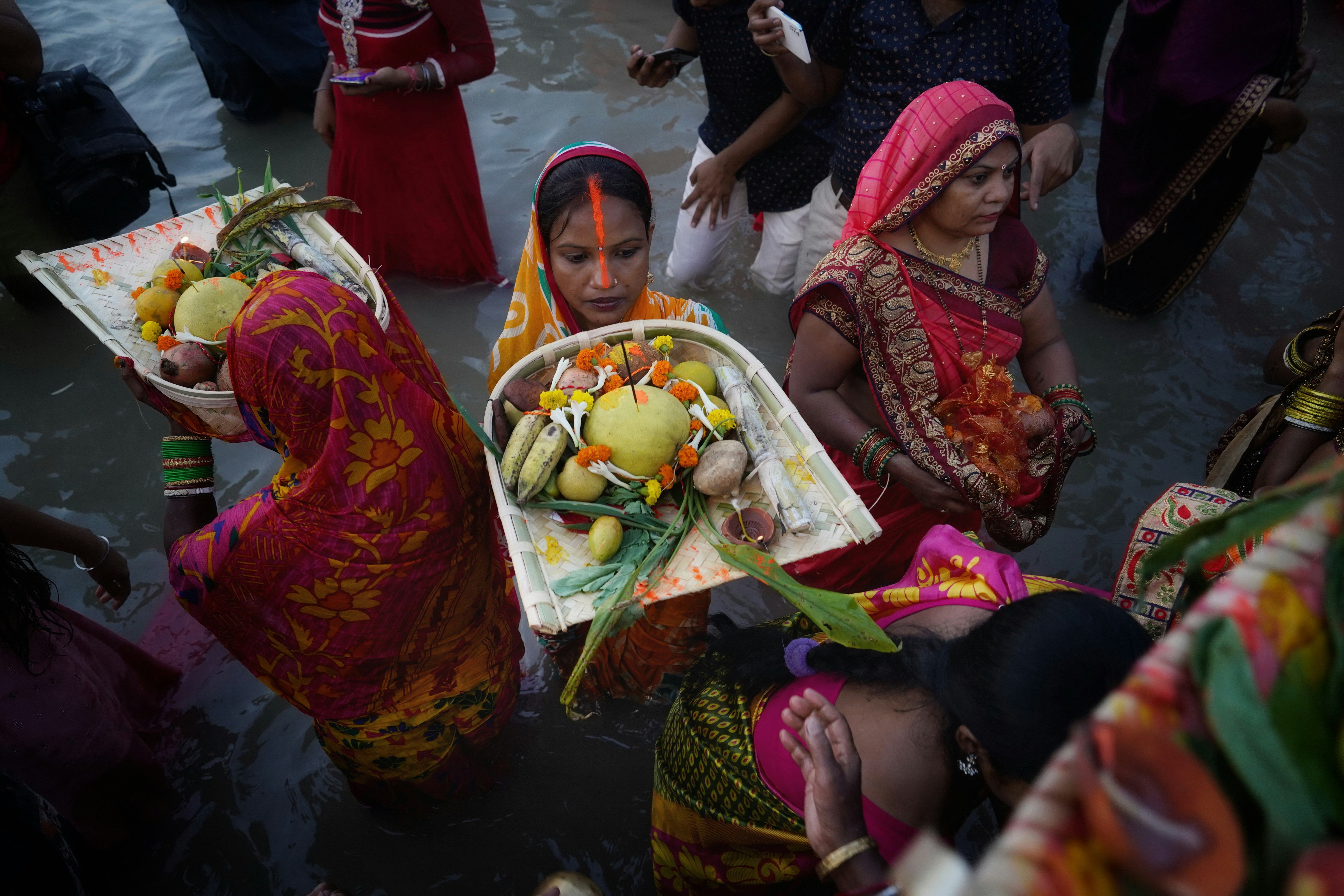 a group of women sitting on the ground with a basket of fruit