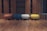 A row of four rounded, modern ottomans in differing colors is arranged on a wooden floor. The background consists of wooden paneling with empty, dark shelves. The ottomans are colored in rust, blue, cream, and yellow tones, adding a pop of color against the neutral backdrop.