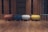 A row of four rounded, modern ottomans in differing colors is arranged on a wooden floor. The background consists of wooden paneling with empty, dark shelves. The ottomans are colored in rust, blue, cream, and yellow tones, adding a pop of color against the neutral backdrop.