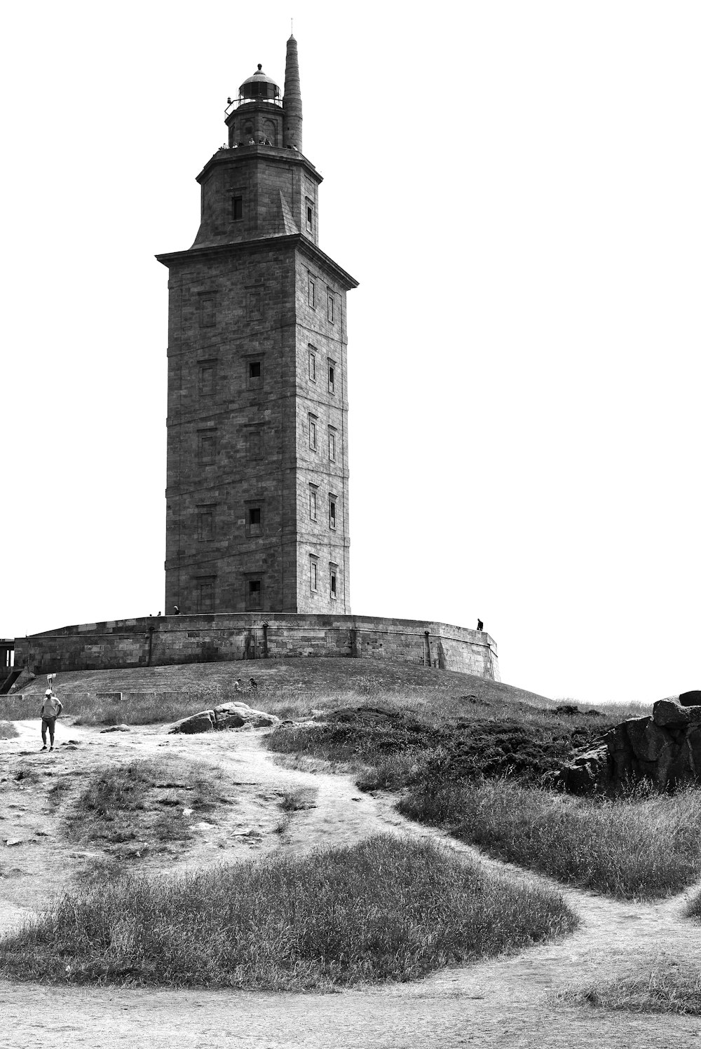 a tall tower with a person walking by it with Tower of Hercules in the background