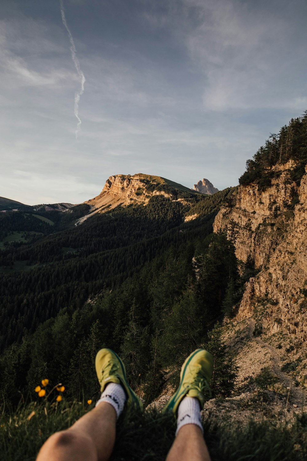 a person's legs and feet on a rock ledge with a mountain in the background