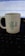 A white ceramic mug with the letter 'P' and the name 'Pravin' printed on it is placed on a keyboard. A computer screen displaying code is visible in the background.