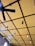 A ceiling features a grid-like pattern with large, alternating squares painted in yellow. There is a black ceiling fan with three blades, and multiple hanging pendant lights with exposed bulbs suspended at different lengths. The architecture presents a modern and stylish design.