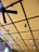 A ceiling features a grid-like pattern with large, alternating squares painted in yellow. There is a black ceiling fan with three blades, and multiple hanging pendant lights with exposed bulbs suspended at different lengths. The architecture presents a modern and stylish design.
