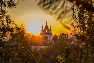 A serene sunset behind a church with worshippers raising their hands in praise.