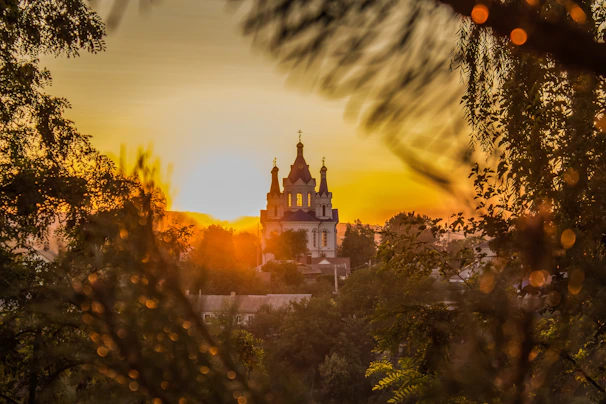 A serene sunset behind a church with worshippers raising their hands in praise.