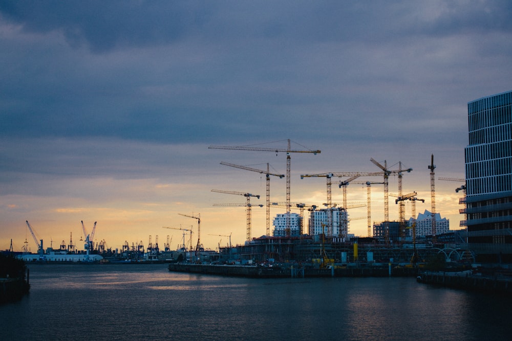 a body of water with cranes and buildings in the background