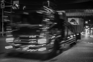 Black and white photo of a tow truck in action at night with bright headlights.