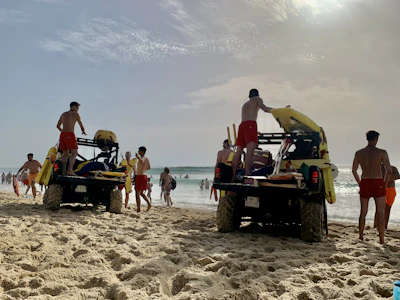 Group of lifeguards smiling and preparing rescue equipment on the sandy beach under a bright blue sky.