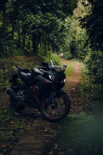 A sleek black motorcycle is parked on a narrow, winding path surrounded by dense, leafy green foliage. The lush greenery creates a tranquil and secluded atmosphere, suggesting a peaceful ride through nature.