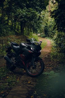A sleek black motorcycle is parked on a narrow, winding path surrounded by dense, leafy green foliage. The lush greenery creates a tranquil and secluded atmosphere, suggesting a peaceful ride through nature.