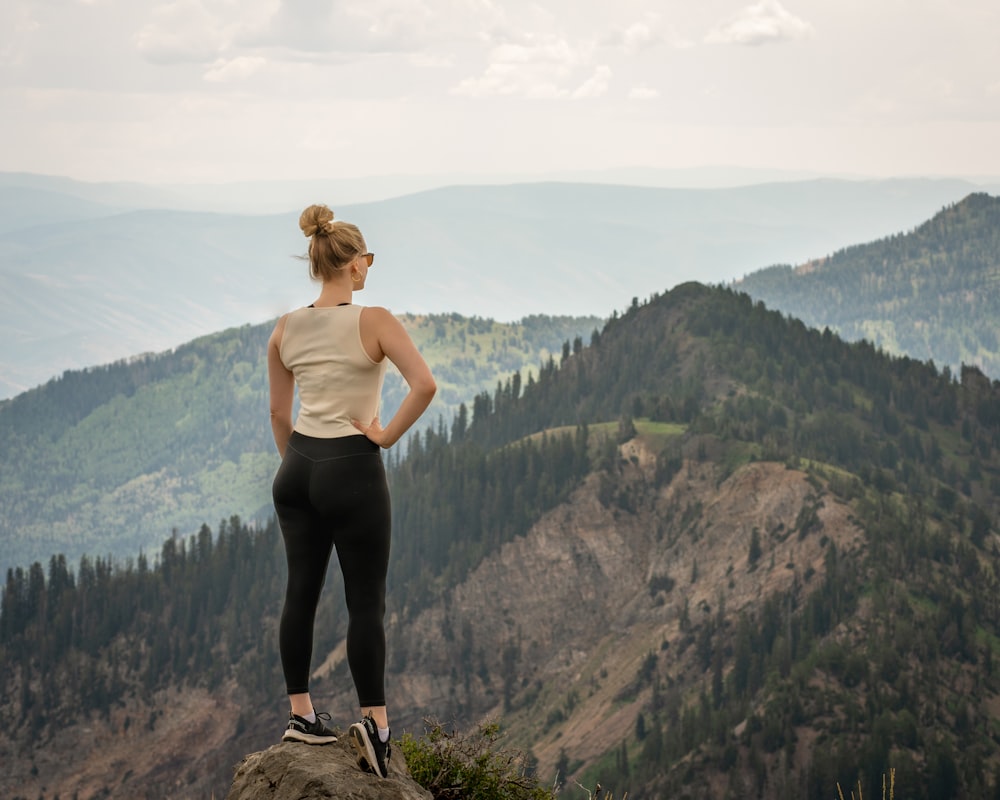 a man standing on a rock overlooking a valley with trees and mountains