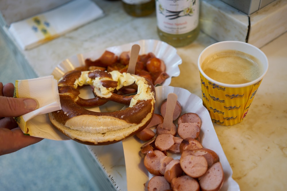 a person holding a cup of coffee next to a burger with a bun