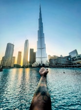 a person's hand reaching out to a body of water with a city in the background