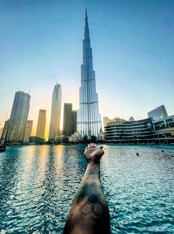 a person's hand reaching out to a body of water with a city in the background