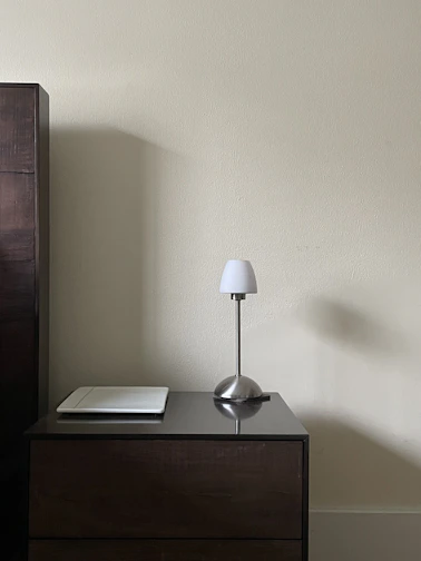 A minimalist floating nightstand beside a cozy bed, featuring a small lamp and a book.
