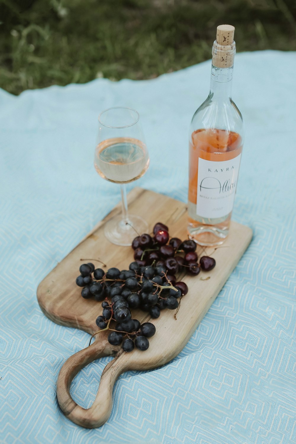 a bottle of wine and grapes on a picnic table