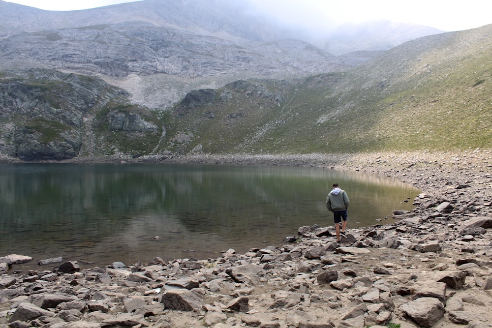 a man standing on a rocky shore by a lake