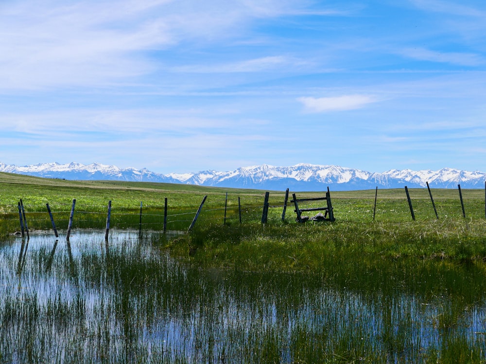 a lake with a fence and snowy mountains in the background