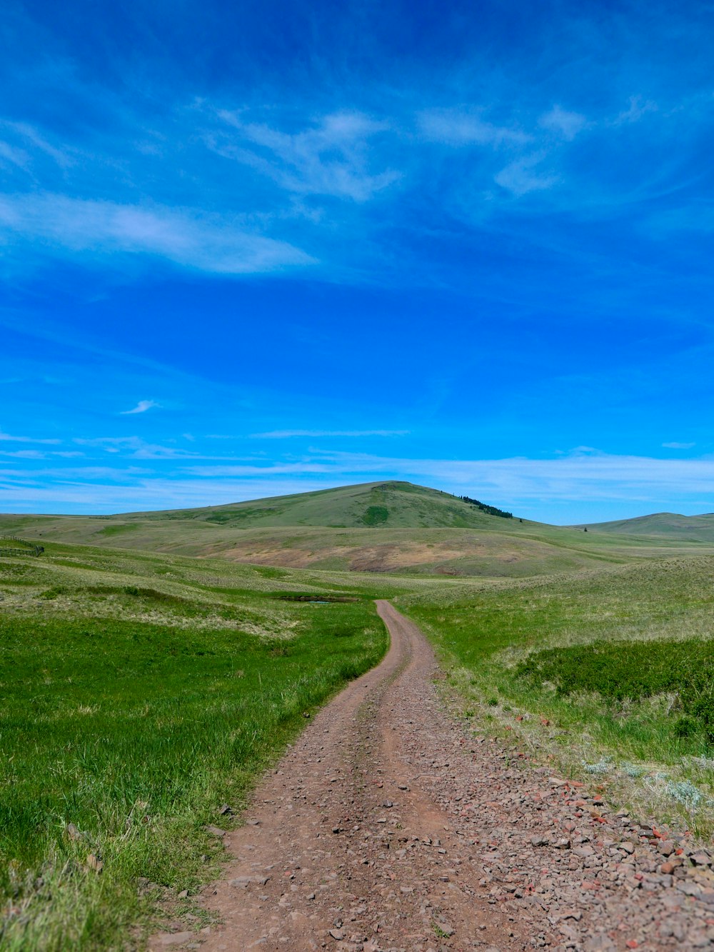 Un camino de tierra que conduce a una colina con una colina cubierta de hierba en el fondo