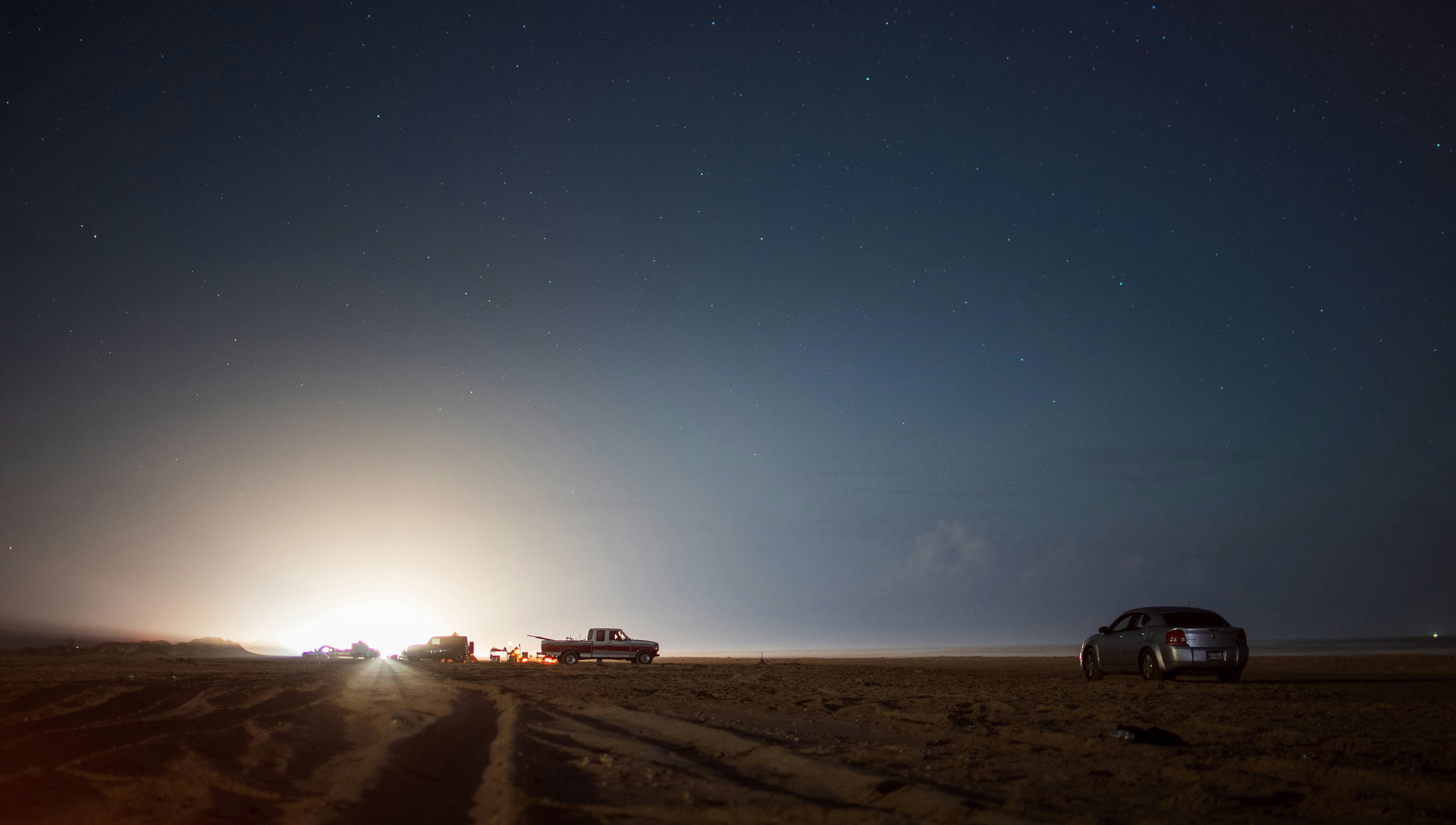 Beach camping at night with tents on sandy shore, stars visible, bonfire glow, dark atmospheric sky