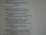 A close-up of a page from a book, specifically showing Psalm 135 with text focused on praise and worship. The text is clearly visible and legible, with a portion emphasized by slightly larger and bold font.