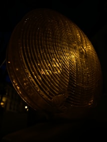 A close-up of a circular amber warning light, displaying a textured surface with concentric patterns. The light emits a warm glow in a dark environment.