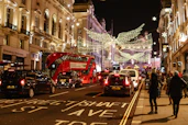 a group of people walk down a sidewalk next to a street with cars and christmas lights