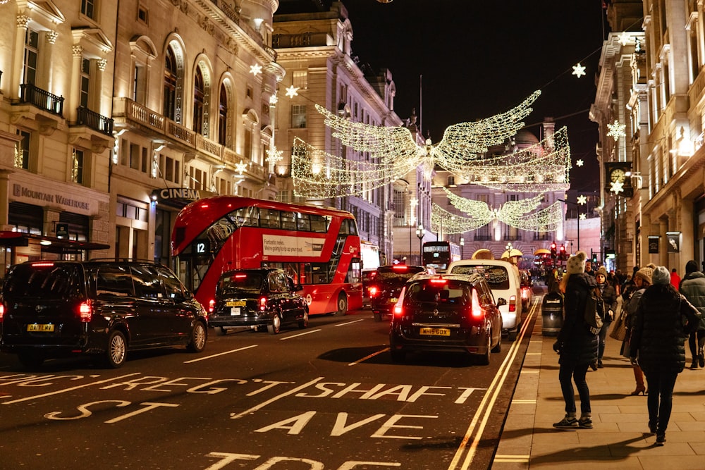 a group of people walk down a sidewalk next to a street with cars and christmas lights