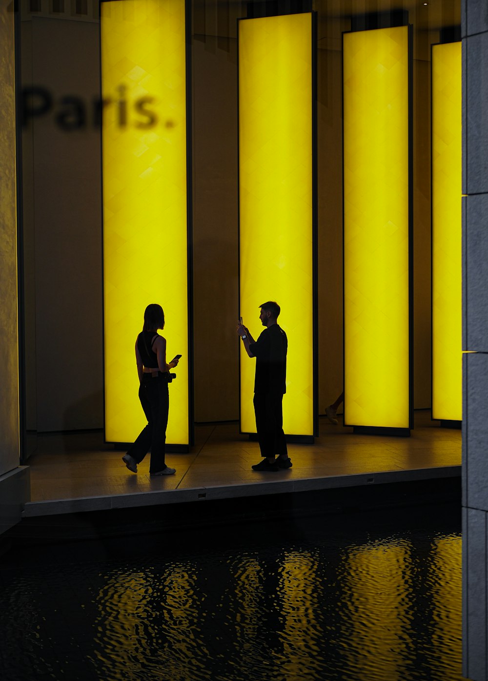 a man and woman standing in a hallway with yellow pillars