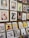 A display of various framed and unframed art pieces on a wooden wall and stands. The artworks include colorful illustrations, abstract designs, and portraits featuring animals, people, and plants. Some pieces are priced at $68 and $69, while others are priced around $29 to $30.
