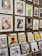 A display of various framed and unframed art pieces on a wooden wall and stands. The artworks include colorful illustrations, abstract designs, and portraits featuring animals, people, and plants. Some pieces are priced at $68 and $69, while others are priced around $29 to $30.