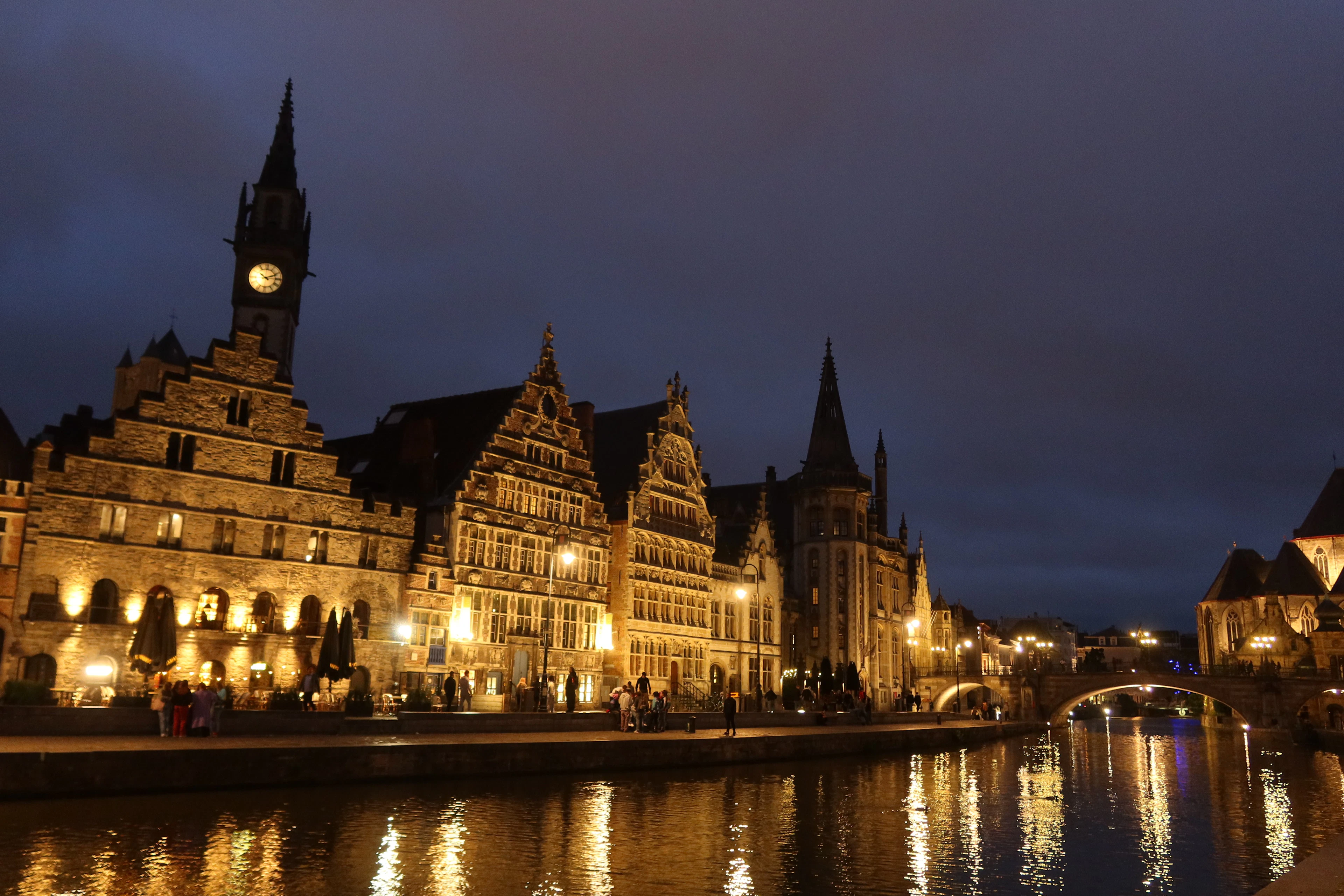 Ghent's Graslei and Korenlei guild houses glowing at night, reflected in the dark canal water.