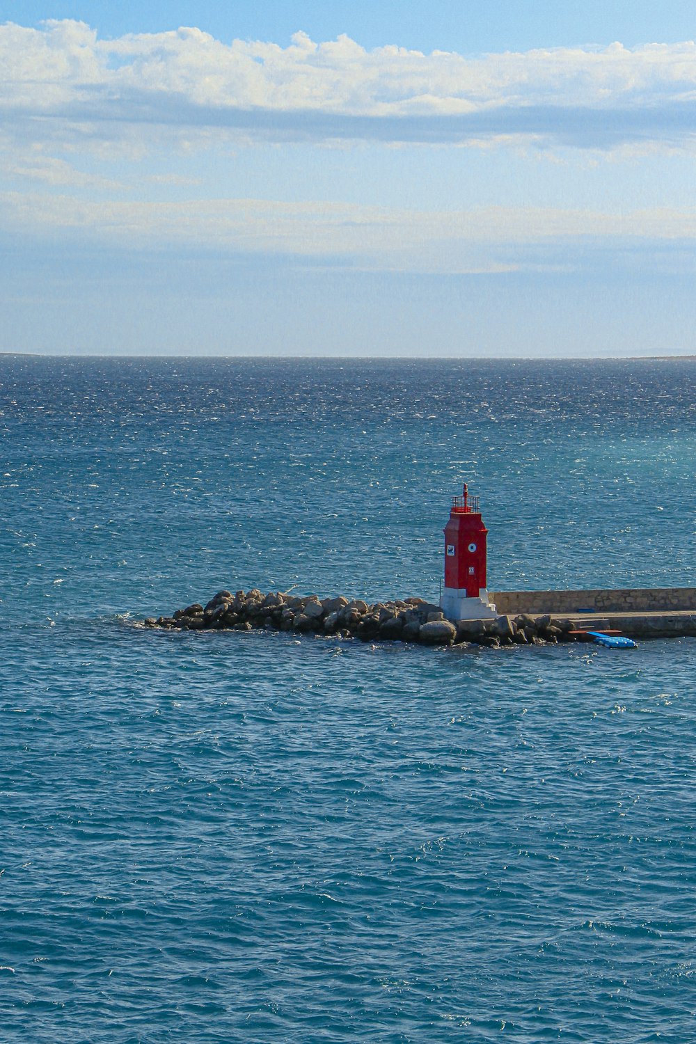 a red light house on a rocky island in the middle of the ocean