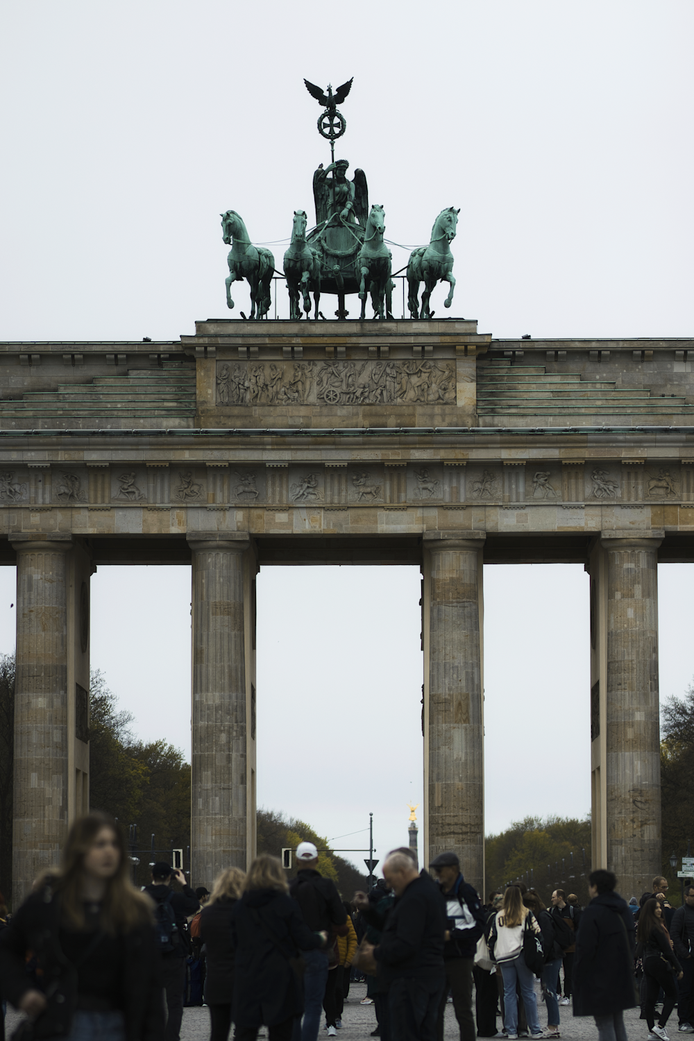 un gruppo di persone in piedi di fronte a un monumento con cavalli in cima con la Porta di Brandeburgo sullo sfondo