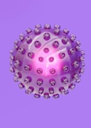 A spherical object resembling a virus or a molecular structure is depicted in a purple hue with protrusions evenly distributed across its surface. The center of the sphere emits a bright pink glow, adding a translucent effect to the sphere.