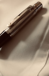 A luxurious pen with metallic accents rests on a smooth, light-colored fabric. The pen's clip has an engraved logo, contributing to its elegant appearance.