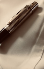 A luxurious pen with metallic accents rests on a smooth, light-colored fabric. The pen's clip has an engraved logo, contributing to its elegant appearance.