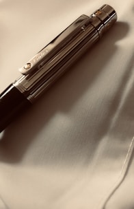 A luxurious pen with metallic accents rests on a smooth, light-colored fabric. The pen's clip has an engraved logo, contributing to its elegant appearance.