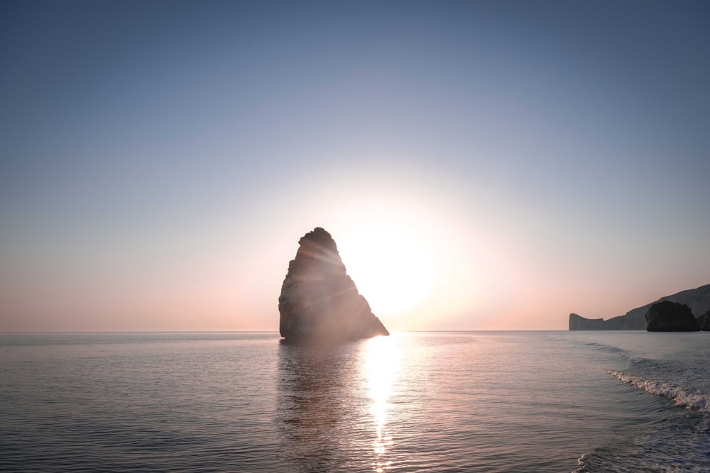 a body of water with a rock in the middle and a blue sky