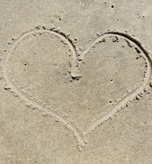 Close-up of a heart drawn in sand on a beach.