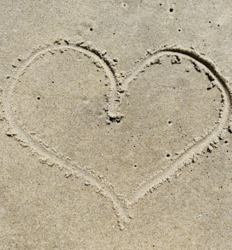 Close-up of a heart drawn in sand on a beach.