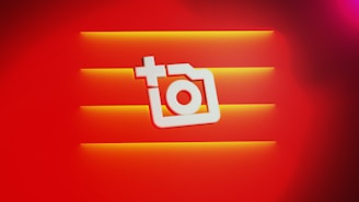 A stylized white camera icon with a plus sign is centered against a vibrant red background. Three horizontal orange stripes provide depth and contrast.