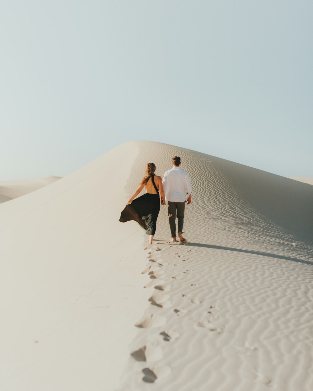 a man and woman walking on a sandy path in the desert